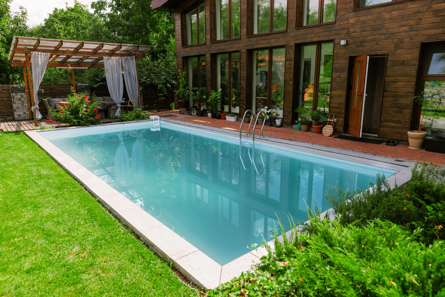 A rectangular garden pool set in a lawn beside a timber-clad house.