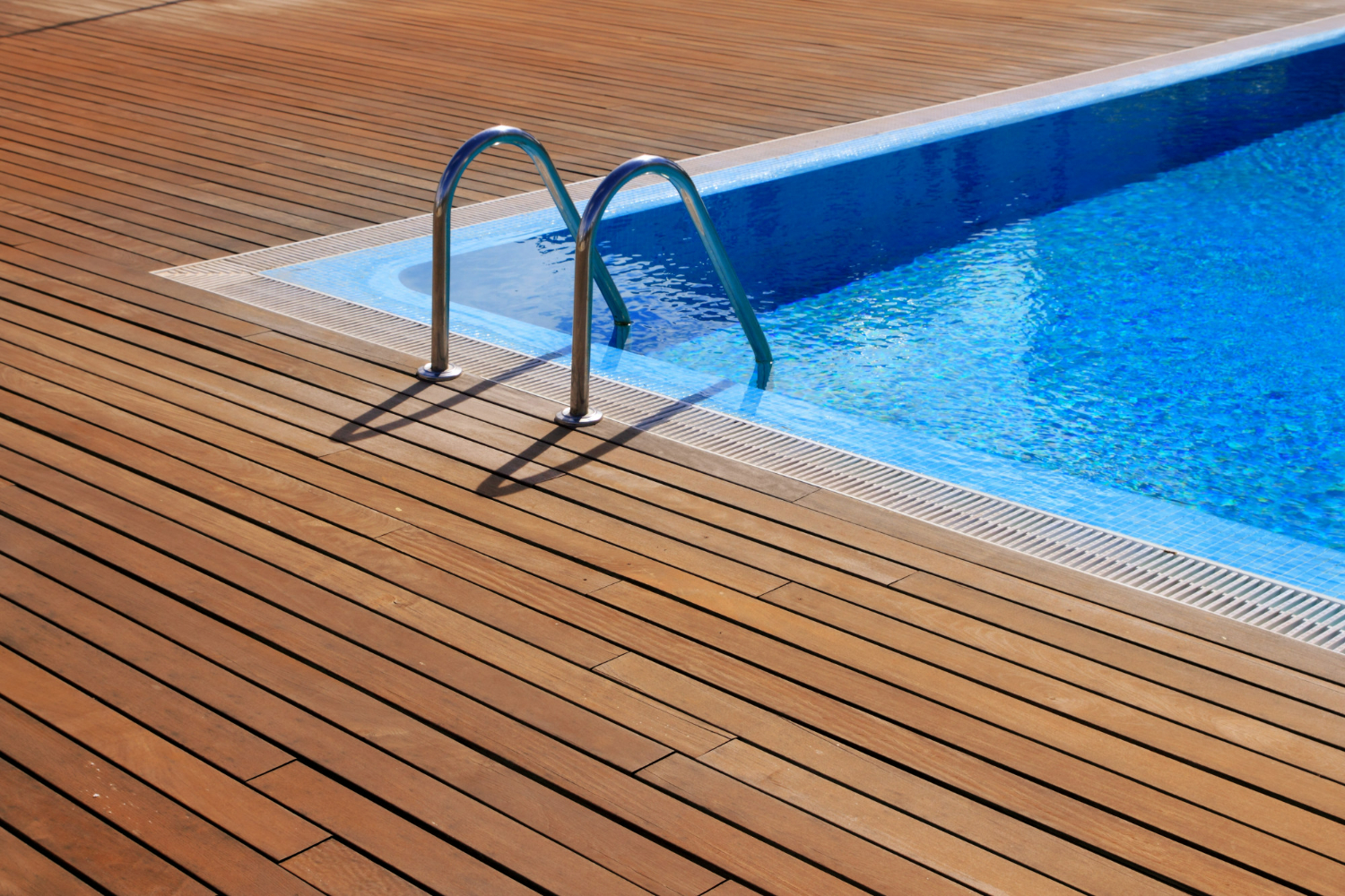 Timber decking meeting a pool edge with a grated overflow channel and steel ladder.