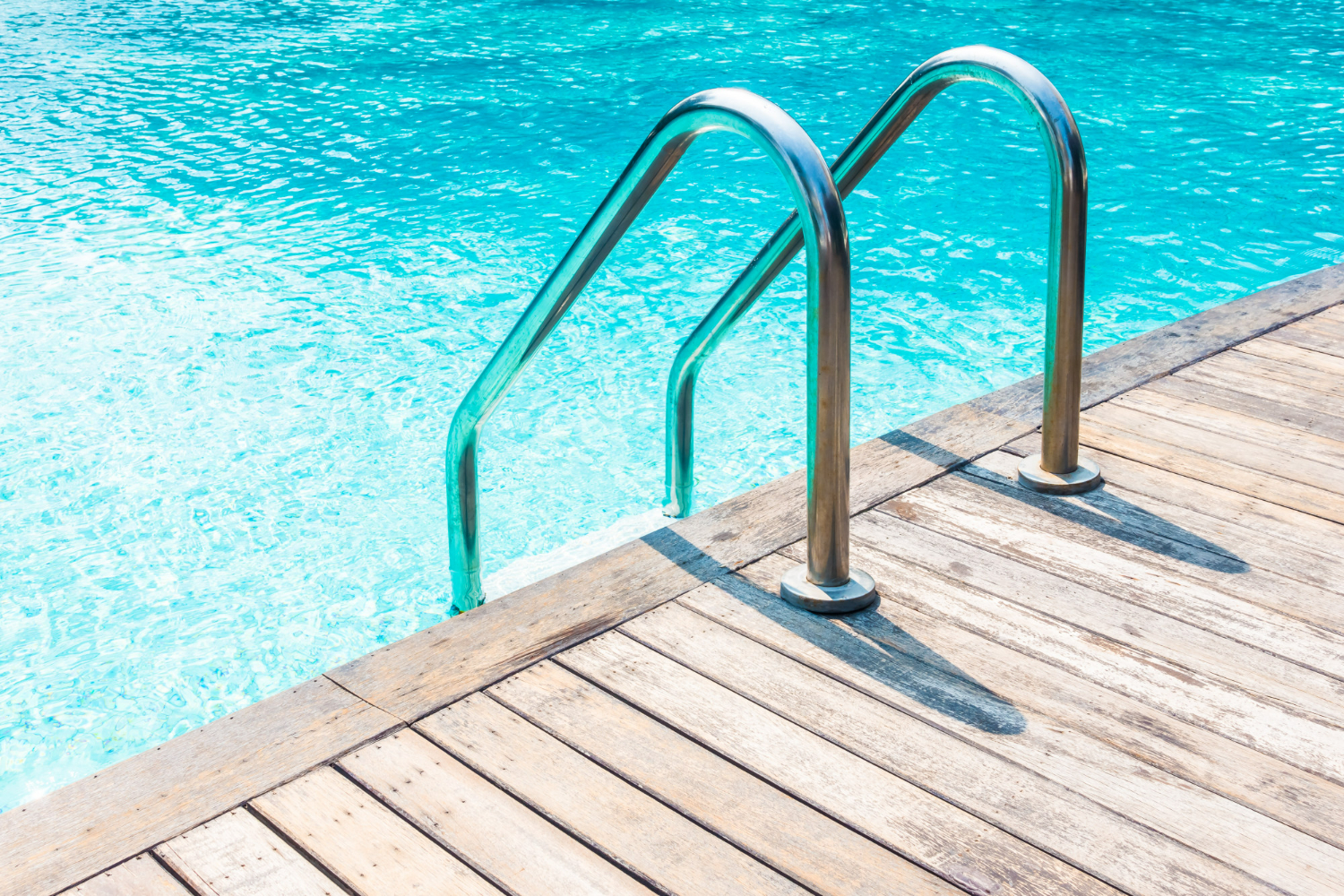 A stainless steel ladder descending from a timber deck into clear pool water.
