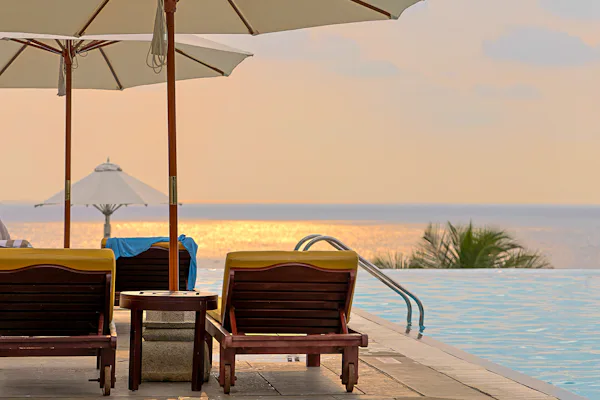Sun loungers and parasols beside a resort pool at sunset.
